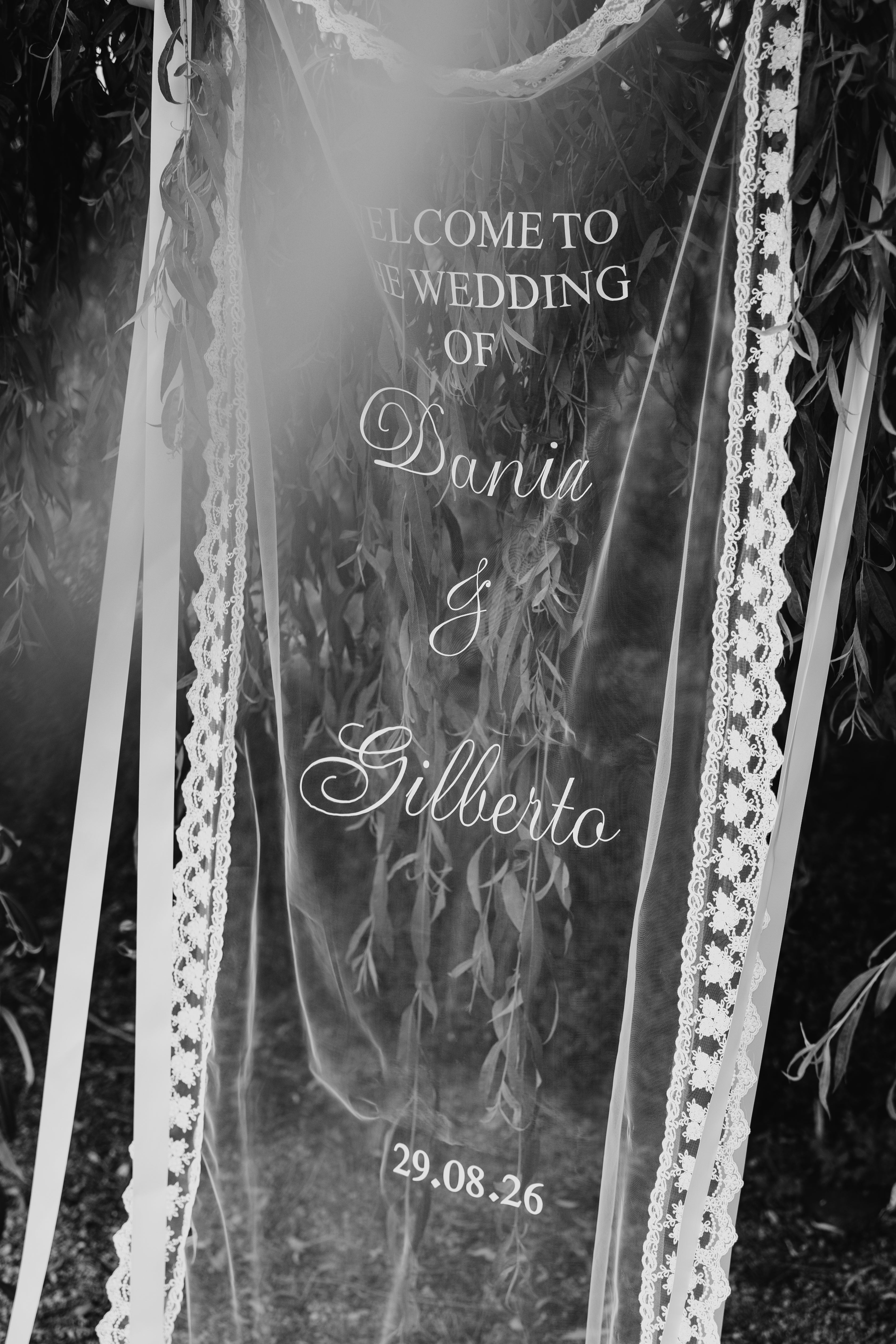 Lace-trimmed hanging wedding sign suspended from a tree, black and white